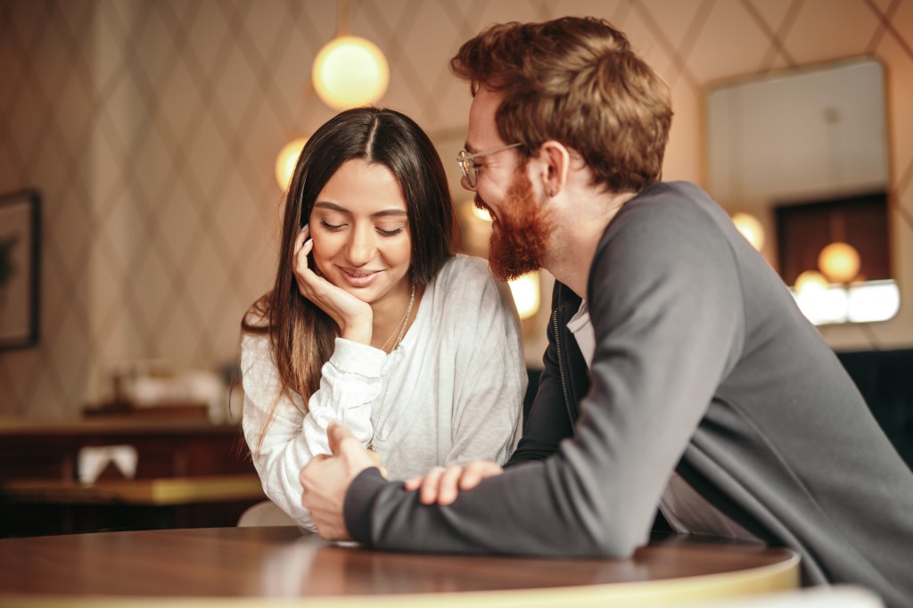 Aaron Ashmore and his young wife, both in elegant clothes, chatting happily and smiling at a cafe table.